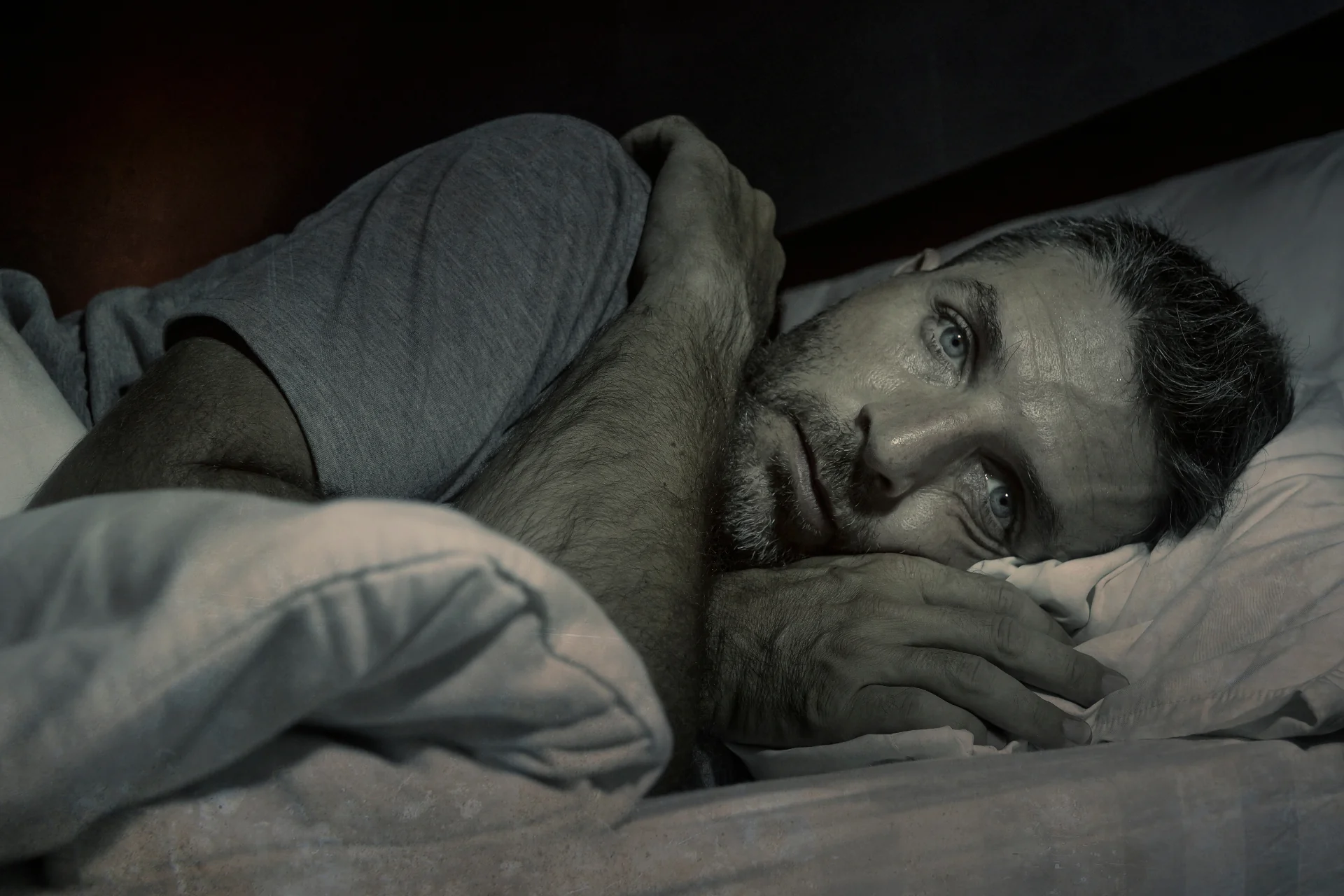 A man lying awake in bed at night, illustrating the struggle with sleeplessness that can weaken immune defenses