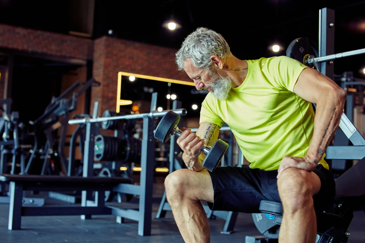 An older man doing dumbbell curls in a gym as part of a prostate cancer exercise routine
